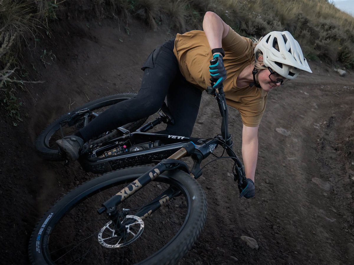 Overhead view of a rider leaning hard into a steep dirt berm on a black Yeti full-suspension mountain bike.