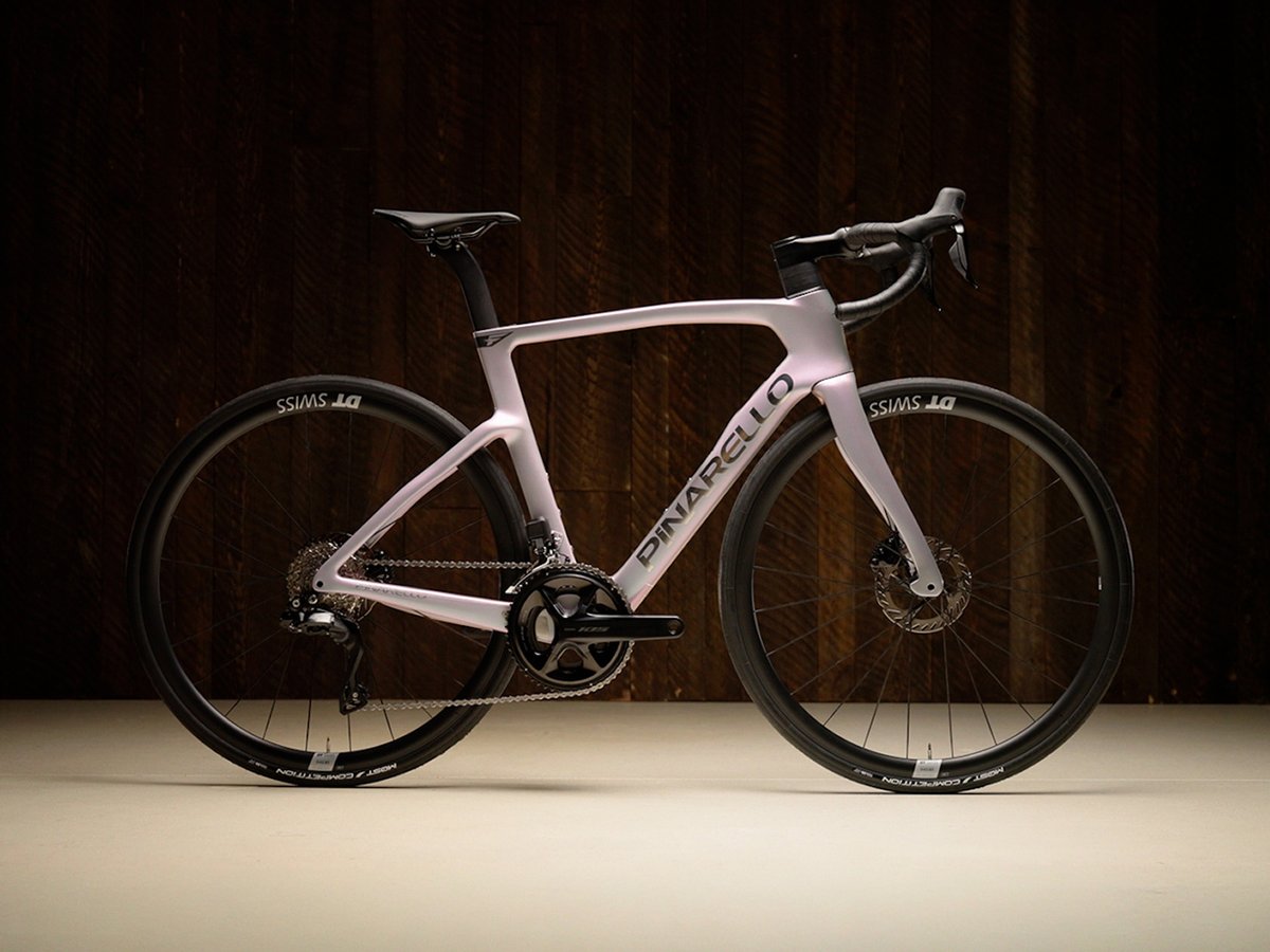 The Pinarello F3 road bike in soft lavender, shown in a side profile against a dark wood background.