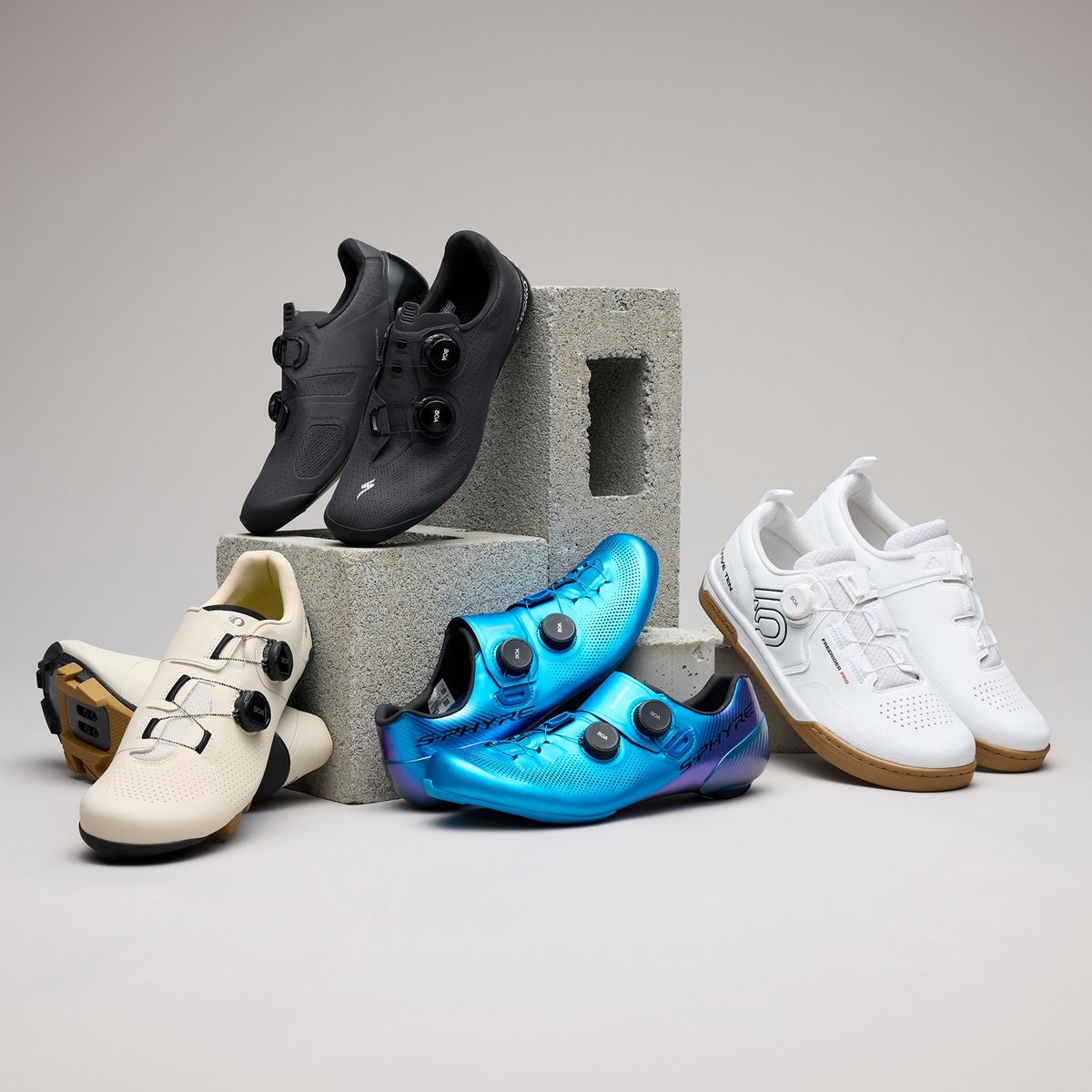 Four pairs of cycling shoes lean against cinder blocks.