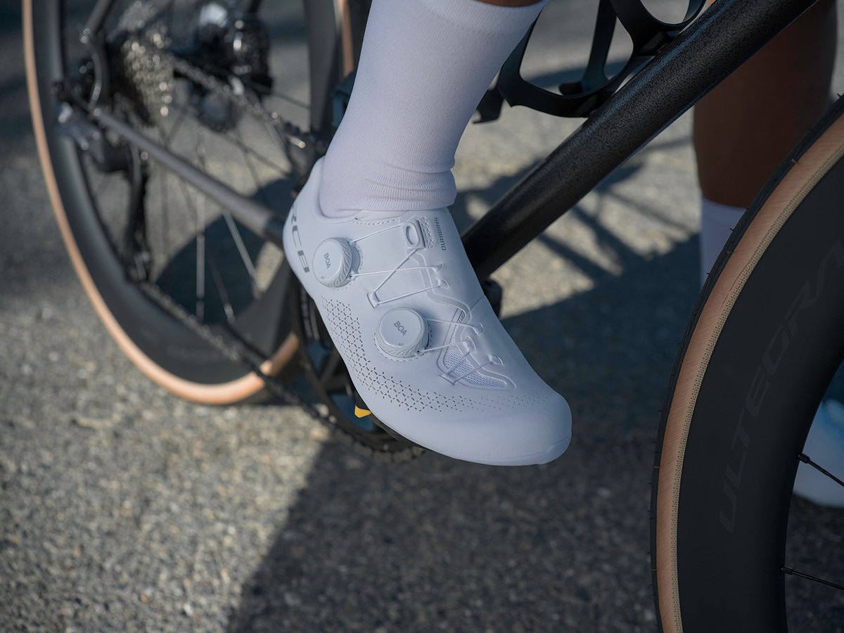 Top-down view of a white RC810 shoe with dual BOA dials clearly visible, cleat visible under the sole, Ultegra-branded tire in frame
