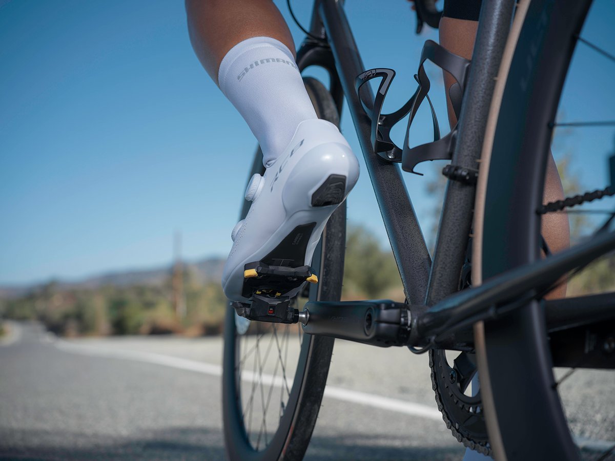 Cyclist's foot in a white RC810 shoe clipped into a pedal, low side-rear angle, black bike frame, road setting