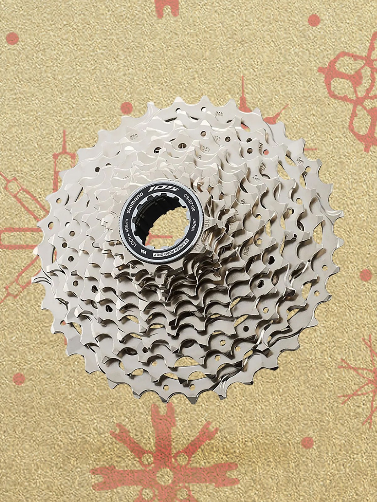 A silver bicycle cassette displayed against a festive gold background with red bike-part snowflake patterns.