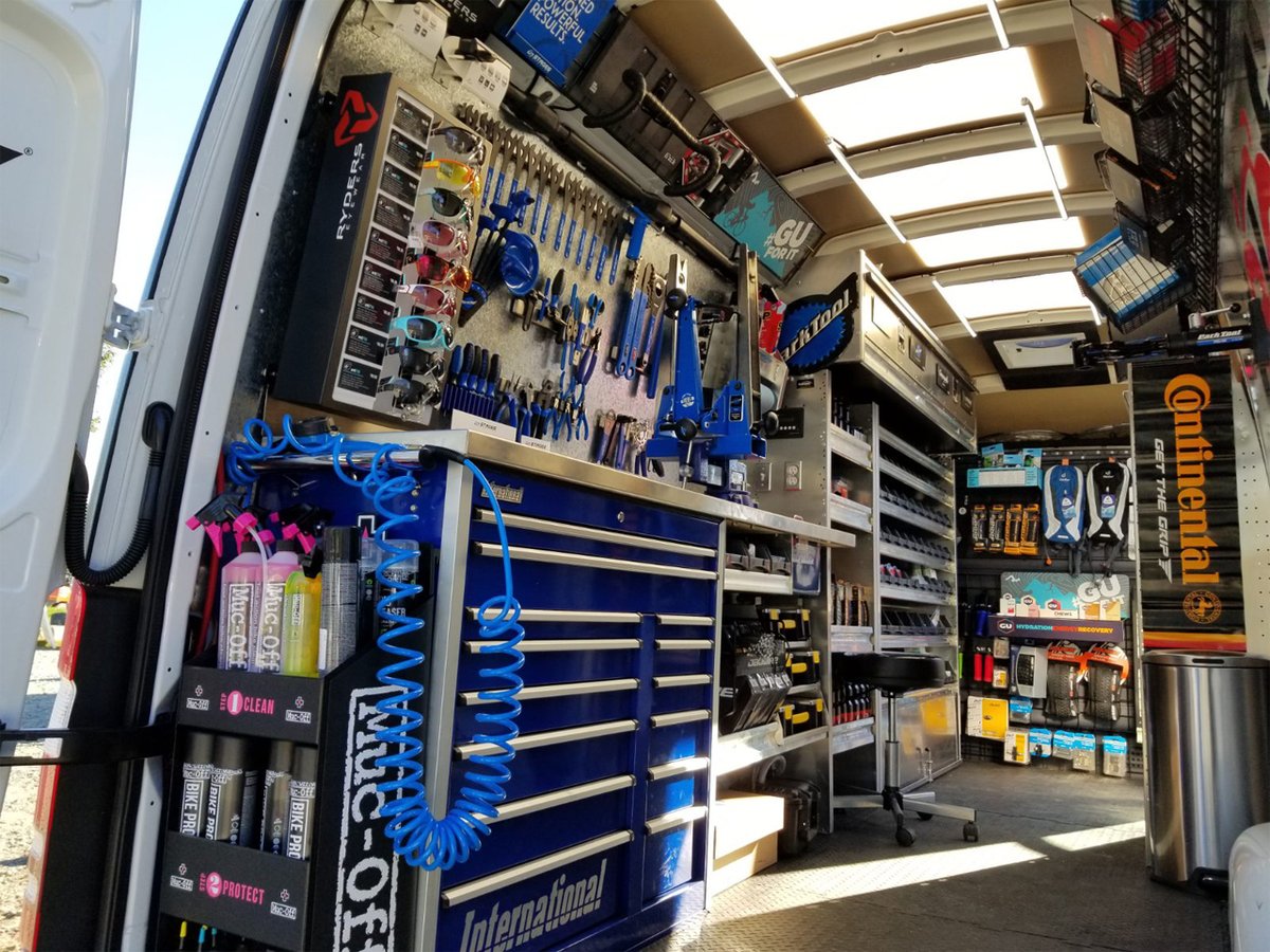 An interior shot of a Velofix van, showing a pro bike work stand, full tool wall, and common parts.