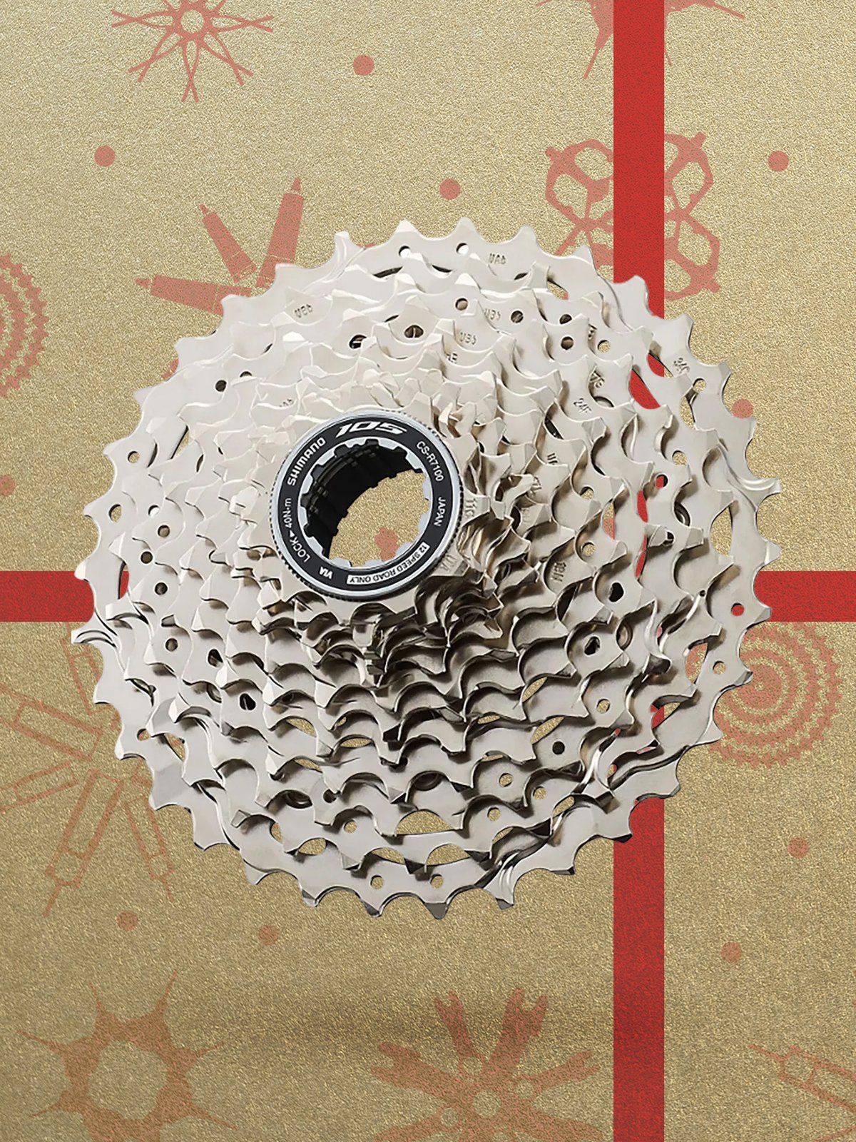 A silver bicycle cassette displayed against a festive gold background with red bike-part snowflake patterns.