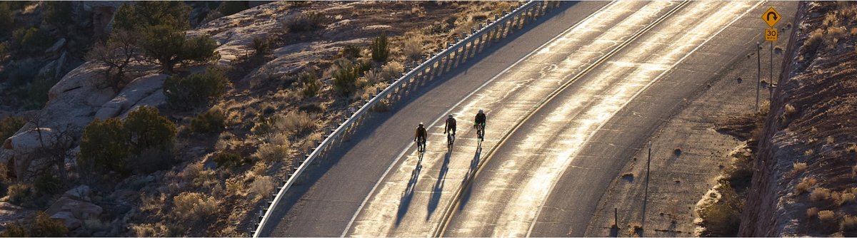 Three riders push the pace on a curved road during golden hour.
