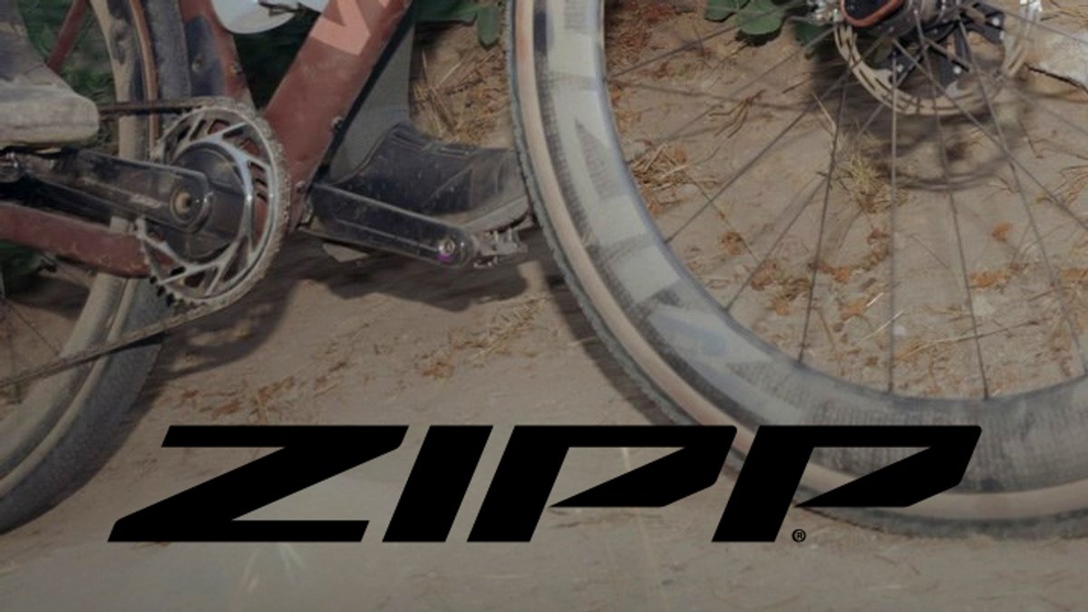 Zipp brand bicycle wheels and drivetrain components displayed on a road bike in sandy outdoor conditions.