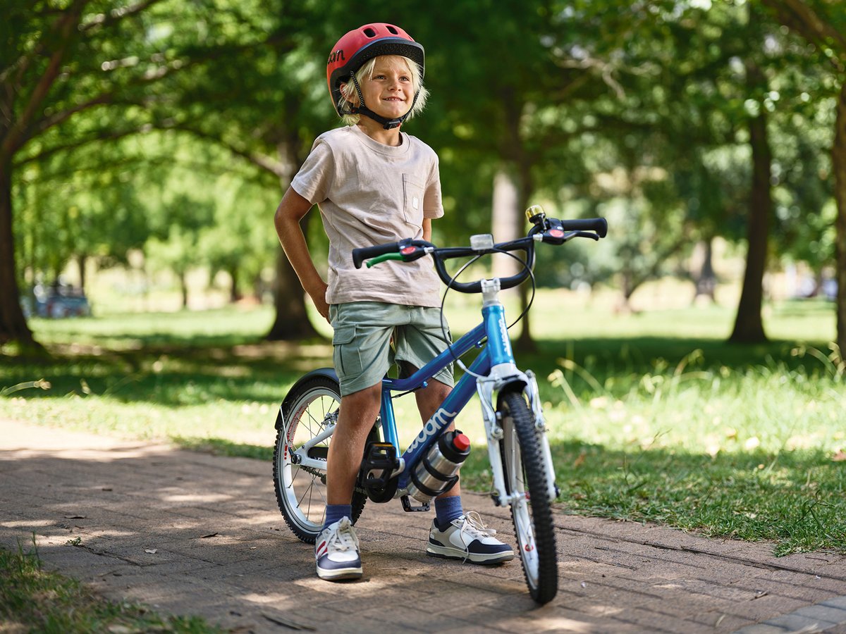 A child straddling a blue woom bike on a tree-lined path.