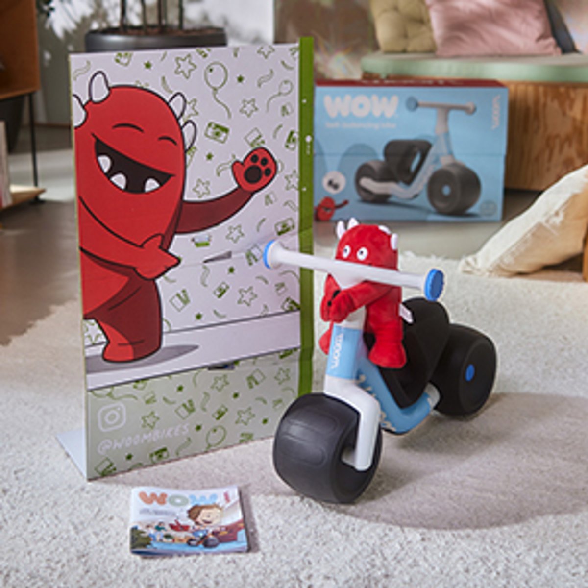 Buddy stuffy riding on the Wow bike with activity book on the floor.
