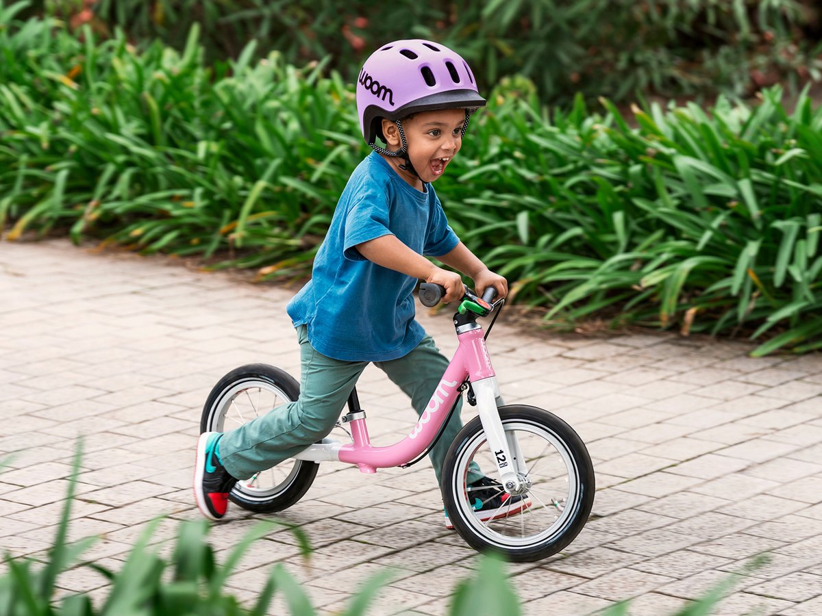 A young child riding a pink woom balance bike on a garden path.