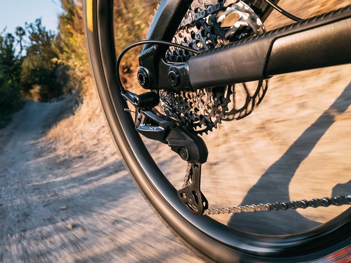 Shimano Deore XT rear derailleur and cassette on a mountain bike in motion on a dirt trail, shot through the rear wheel.