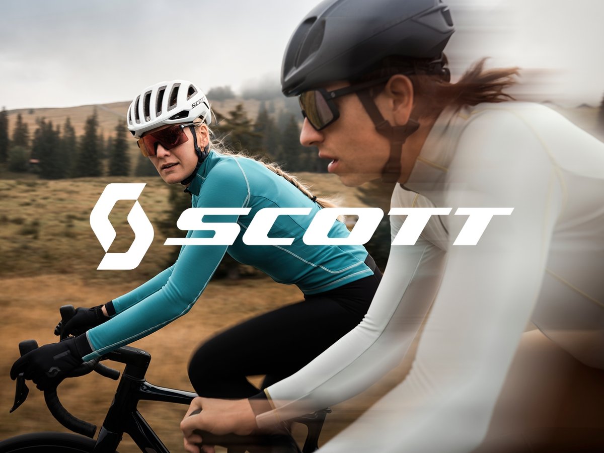 Two cyclists blur past the landscape. Text overlay reads: Now Riding Scott.