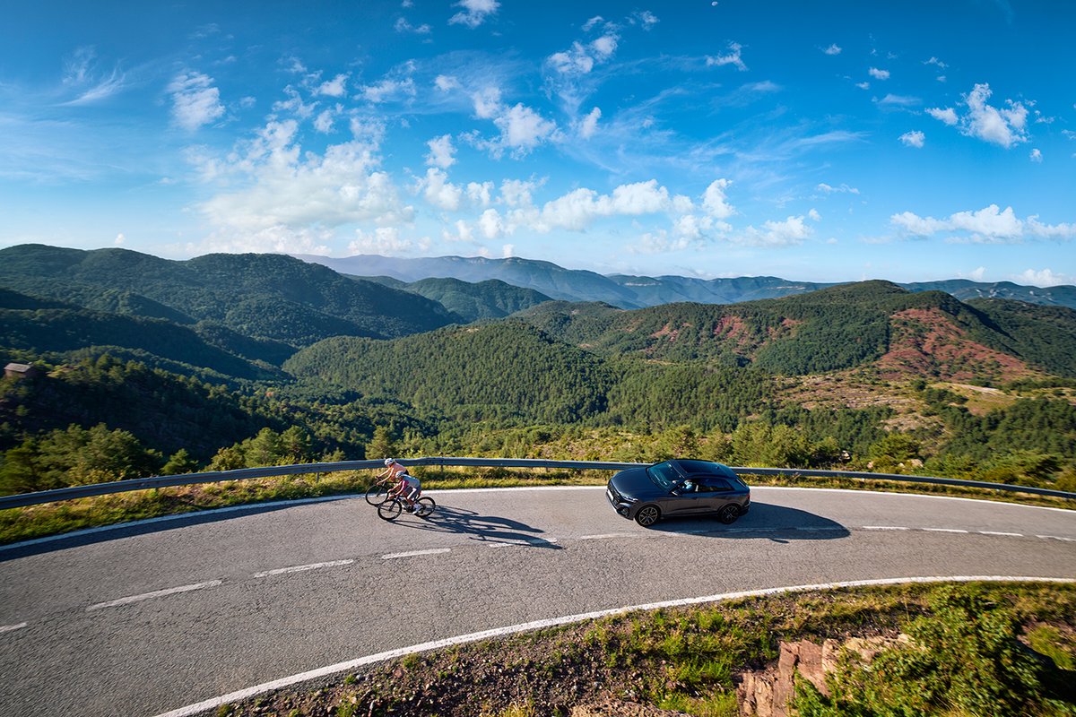 Road cyclists riding mountain pass with car approaching from behind