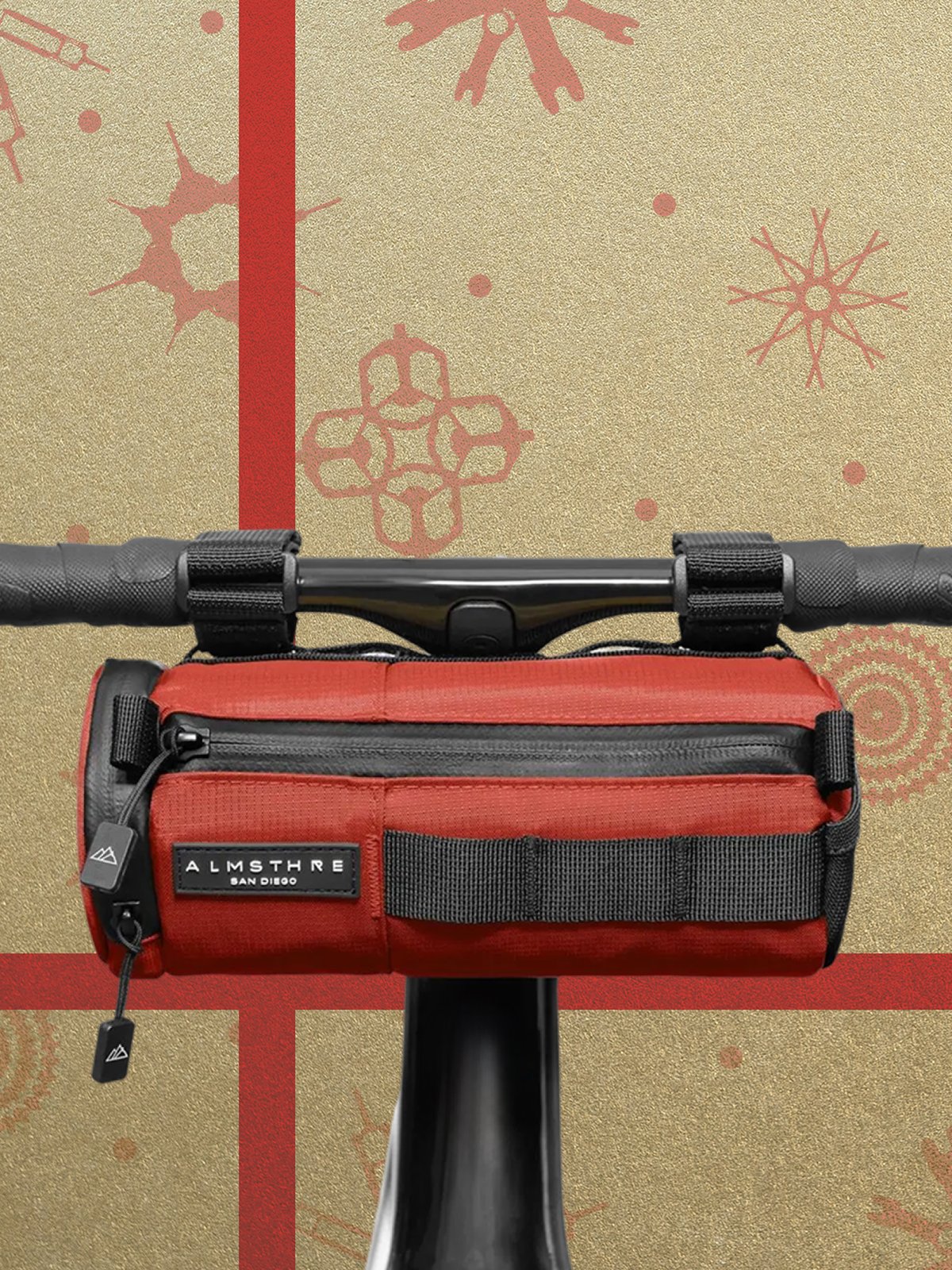 A red handlebar bag labeled "Almsthre" attached to the handlebars of a bicycle, with a bike themed wrapping paper background.