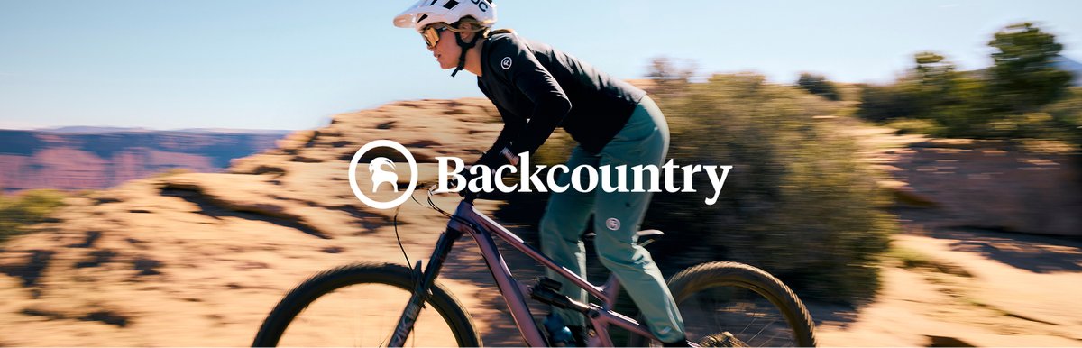 A mountain biker wearing a black long-sleeve jersey and teal riding pants blurs behind the Backcountry logo.
