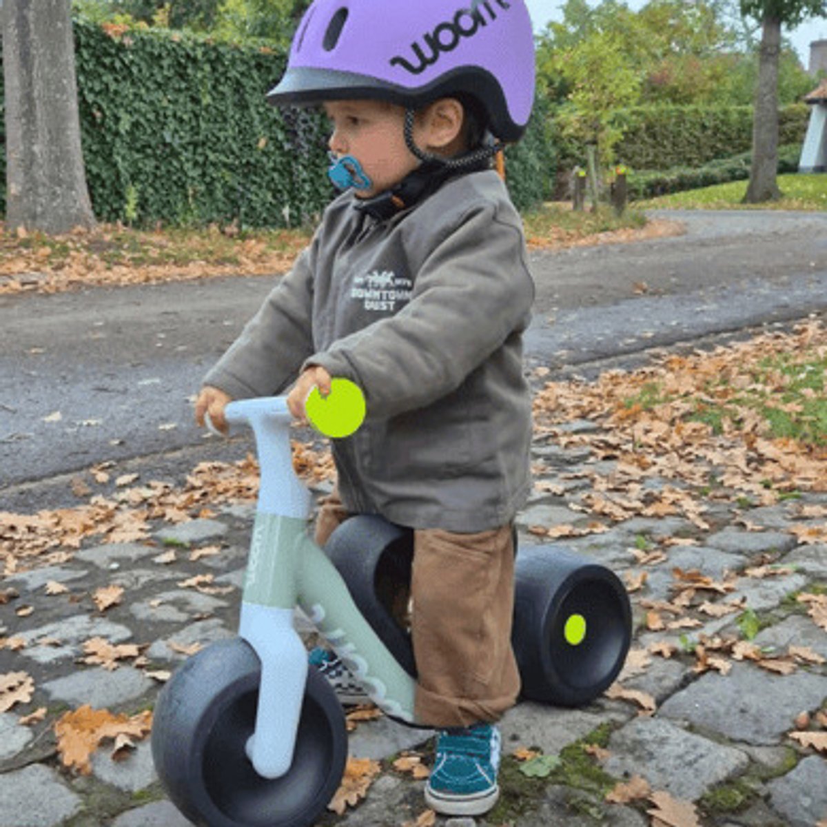 Young kid wearing helmet riding Wow bike on cobblestone surface.