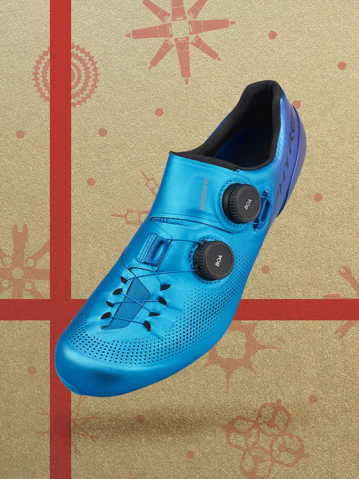 A metallic blue cycling shoe with two BOA dial closures displayed against gold and red wrapping paper.