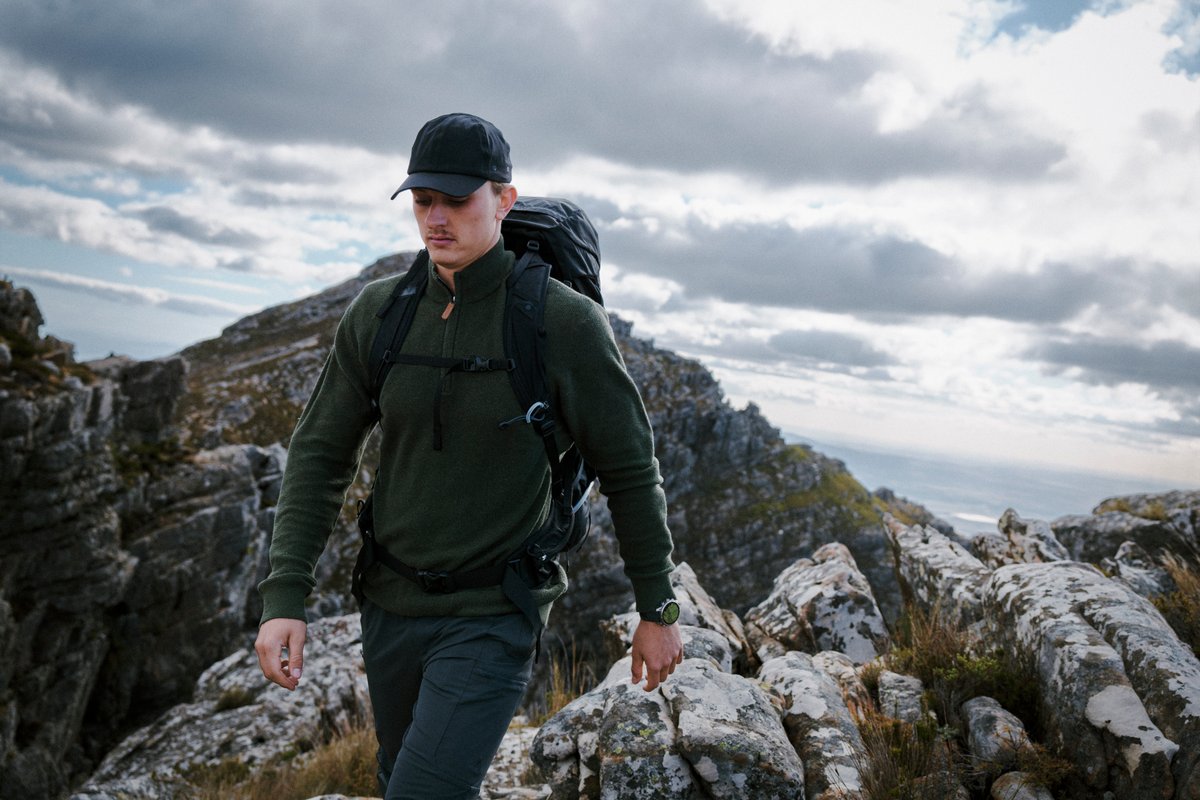Person hiking on mountain ridge wearing Garmin Fenix 9 watch.