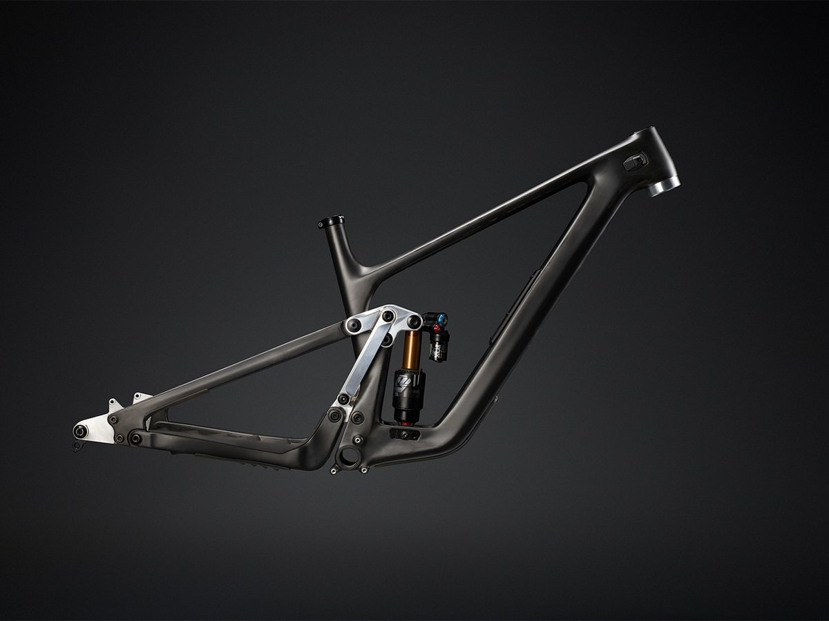 Unpainted prototype carbon frame in profile, showing the Sixfinity linkage and shock mount with raw carbon finish and exposed frame welds.