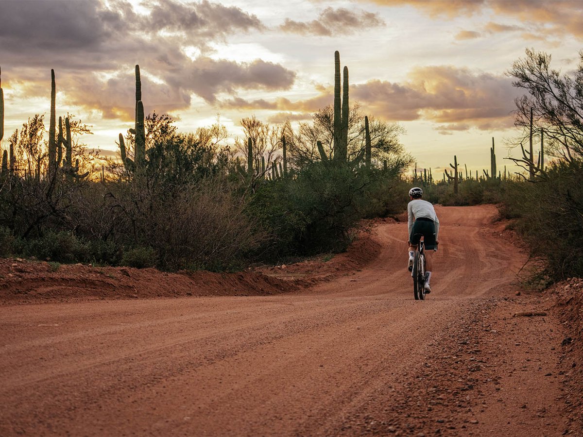 Gravel rider riding away down a dirt road in the desert.